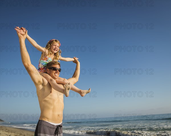 Caucasian father carrying daughter on beach