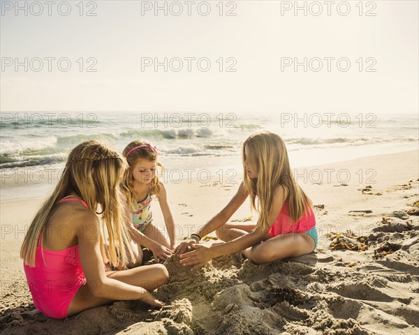 Caucasian sisters building sandcastle on beach