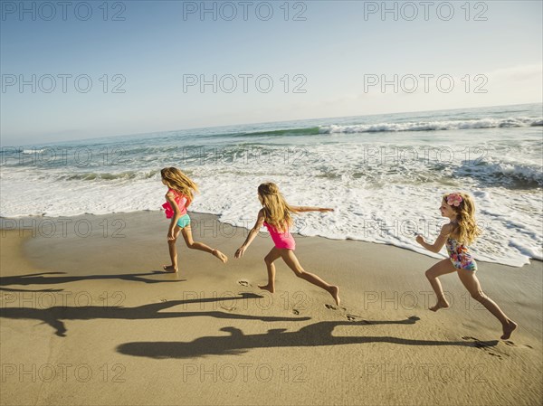 Caucasian sisters running on beach