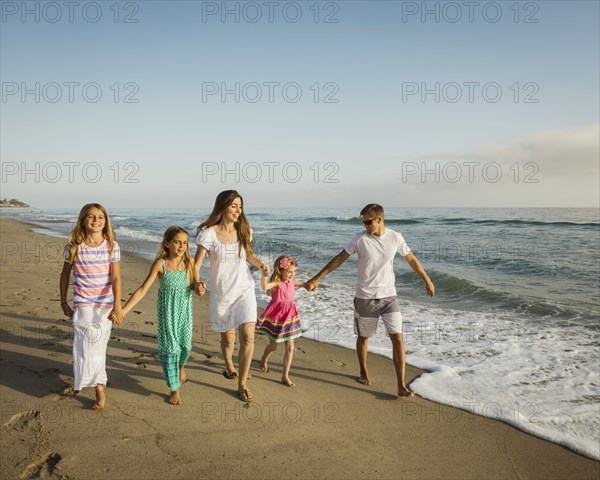 Caucasian family holding hands on beach