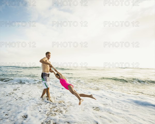Caucasian father and daughter playing in waves on beach