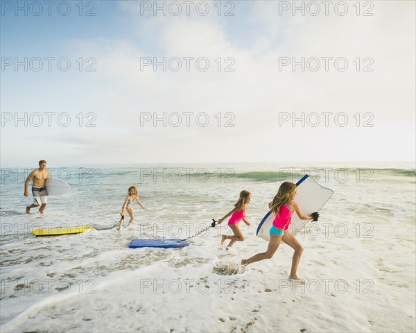 Caucasian father and daughters playing in waves on beach