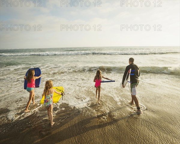 Caucasian father and daughters playing in waves on beach