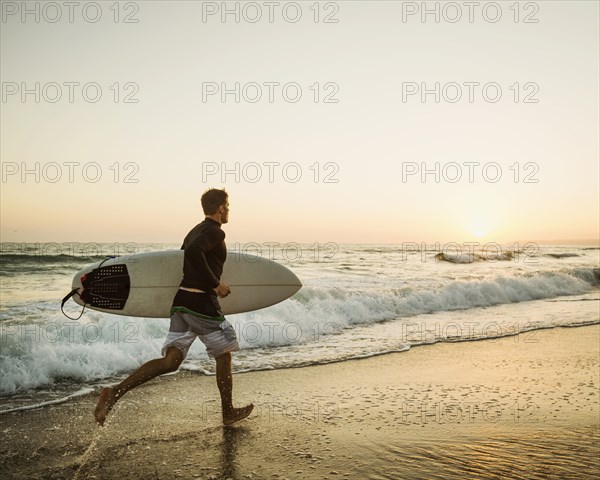 Caucasian man carrying surfboard on beach