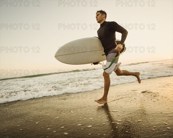 Caucasian man carrying surfboard on beach