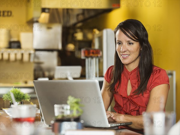 Hispanic businesswoman using laptop in cafe