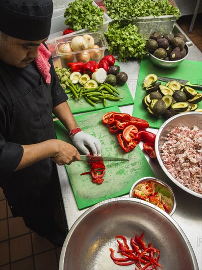 Hispanic chef cutting vegetables in kitchen