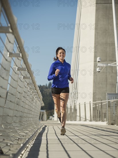 Caucasian woman jogging on urban bridge