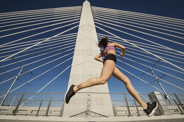 Low angle view of Caucasian woman jogging on urban bridge