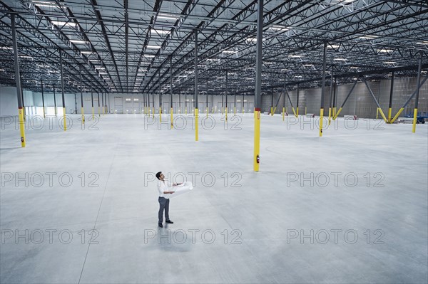 Indian architect holding blueprint in empty warehouse