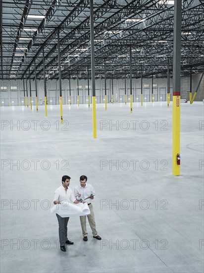 Architects examining blueprint in empty warehouse
