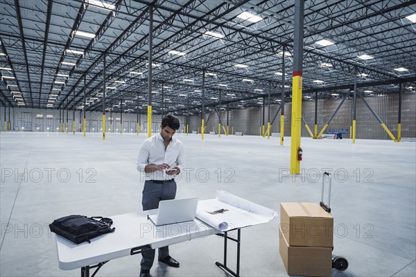 Indian architect texting on cell phone in empty warehouse