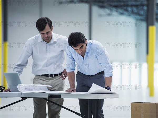 Architects using laptop and blueprint in warehouse