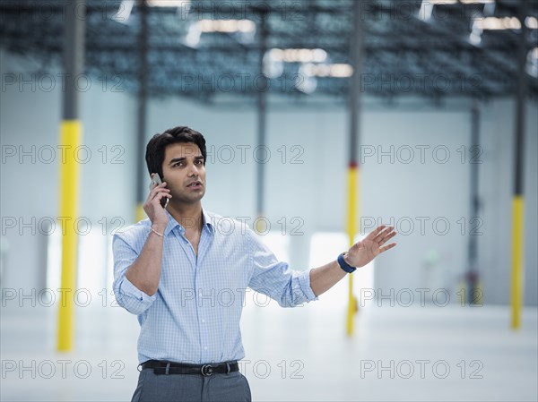 Indian businessman talking on cell phone in empty warehouse