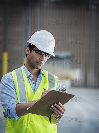 Smiling Indian worker writing on clipboard in empty warehouse