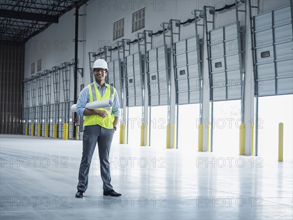 Smiling Indian architect holding blueprint near open loading dock doors