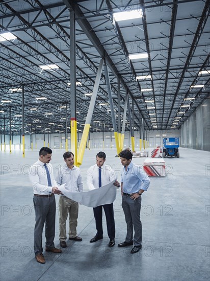 Architects examining blueprint in empty warehouse