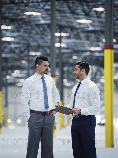 Businessmen with clipboard talking in empty warehouse