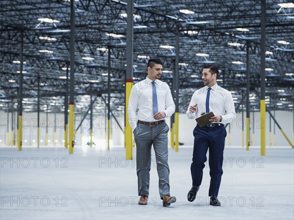 Businessmen with clipboard talking in empty warehouse