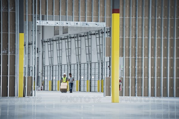 Workers with boxes on hand truck in empty warehouse