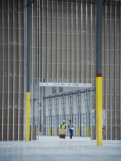 Workers with boxes on hand truck in empty warehouse