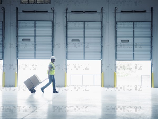 Indian worker pulling hand truck near open loading dock doors