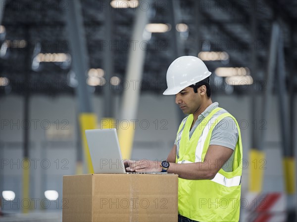 Indian worker using laptop on cardboard box in warehouse