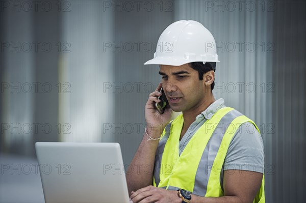 Indian worker using laptop and cell phone in warehouse