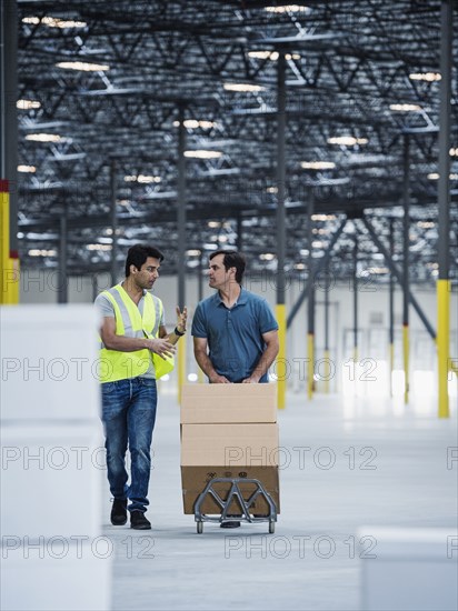 Workers pushing cardboard boxes on hand truck in warehouse