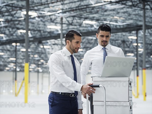 Businessmen using laptop on cardboard boxes in warehouse