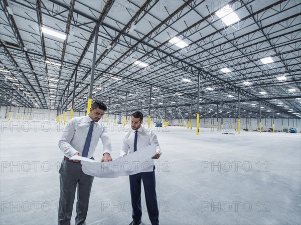 Architects examining blueprint in empty warehouse