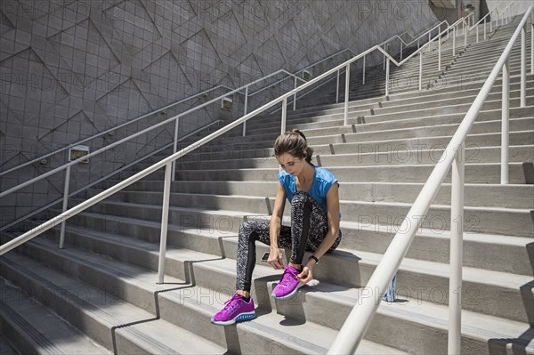 Caucasian woman sitting on staircase tying shoelace