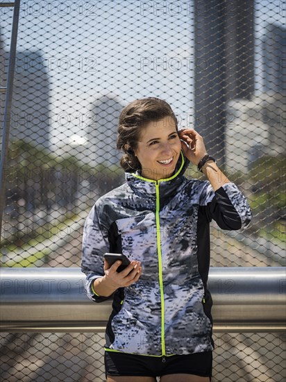 Caucasian woman leaning on bridge railing listening to earbuds