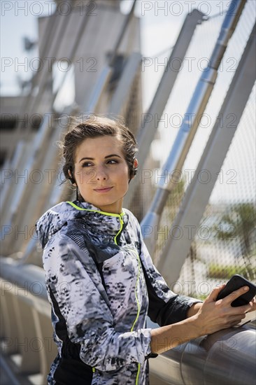 Caucasian woman leaning on bridge railing listening to earbuds