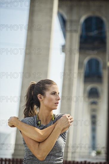 Caucasian woman stretching arms under overpass