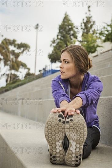 Caucasian woman stretching legs on stadium staircase