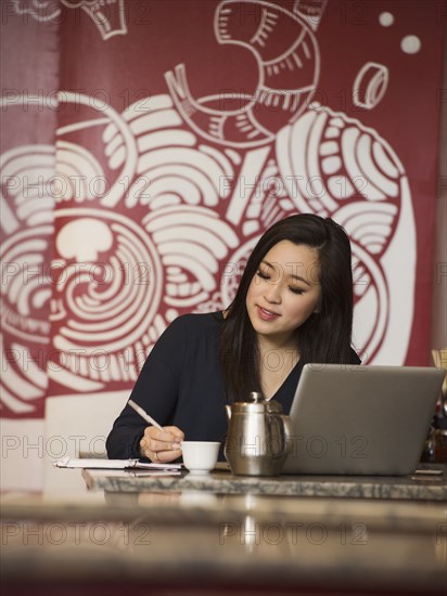 Chinese businesswoman writing in notebook in restaurant