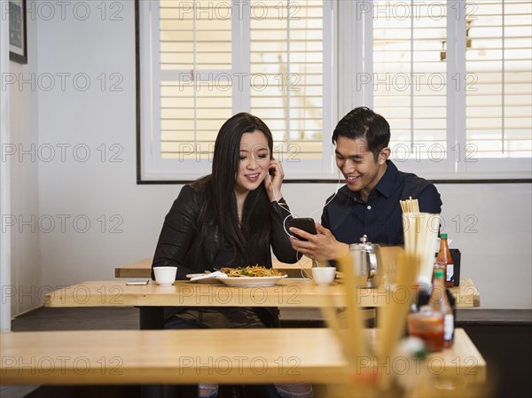 Smiling Chinese couple listening to cell phone in restaurant