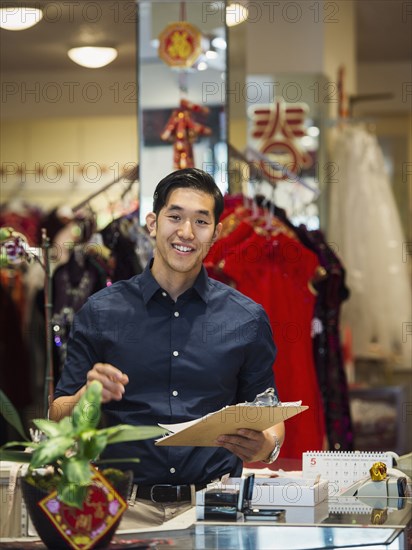 Smiling Chinese man writing on clipboard in store