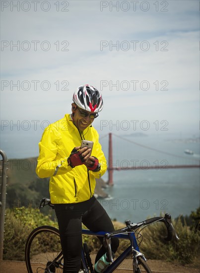 Hispanic man on bicycle texting on cell phone at waterfront