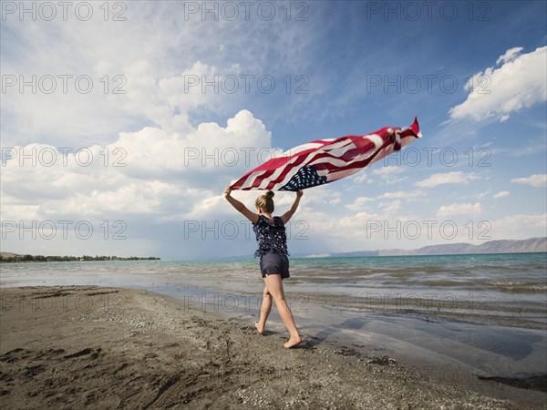 Caucasian girl walking with American flag at beach