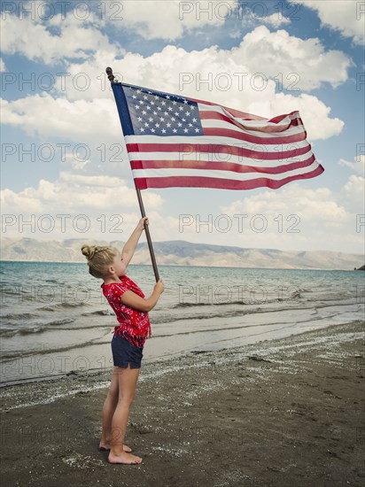 Caucasian girl holding American flag at beach