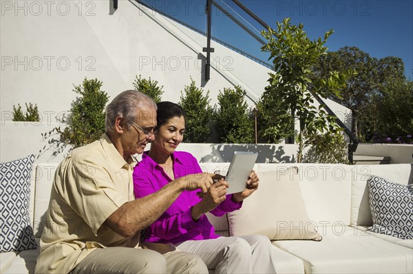 Older couple using digital tablet on modern backyard patio