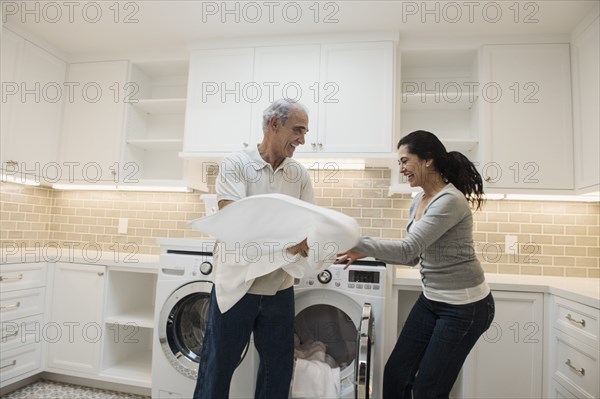 Playful couple folding towel in modern laundry room