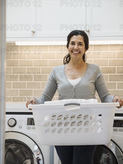 Hispanic woman carrying basket in modern laundry room