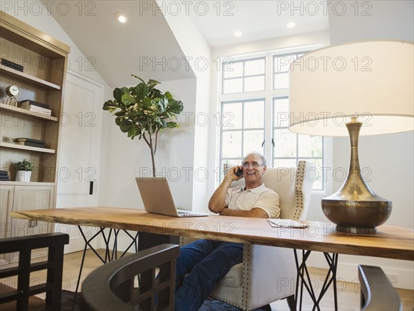 Caucasian man talking on cell phone in home office