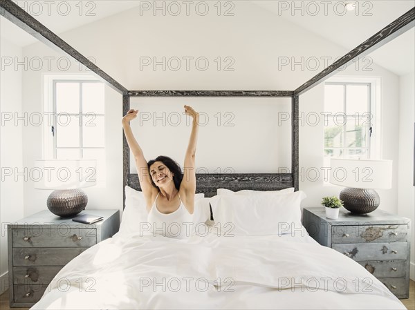 Hispanic woman stretching arms in bed