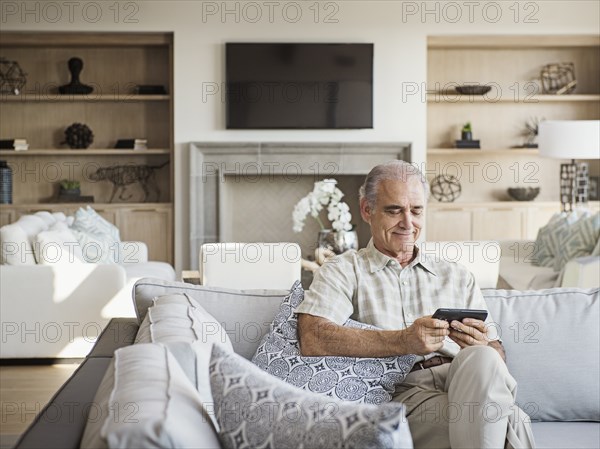 Caucasian man sitting on sofa texting on cell phone