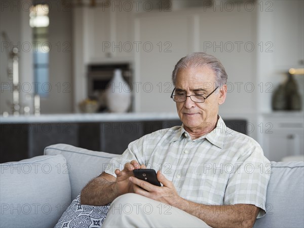 Caucasian man sitting on sofa texting on cell phone