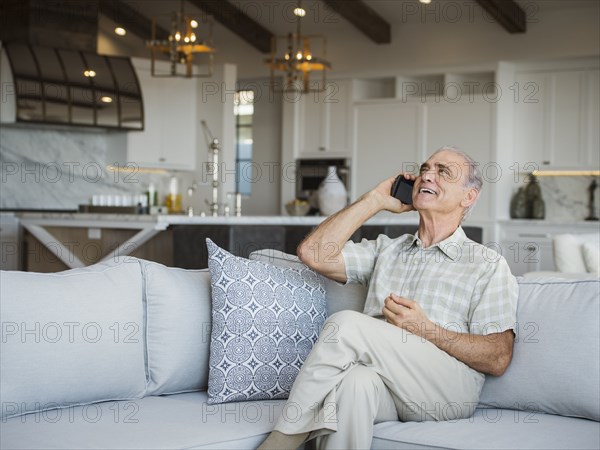 Caucasian man sitting on sofa talking on cell phone